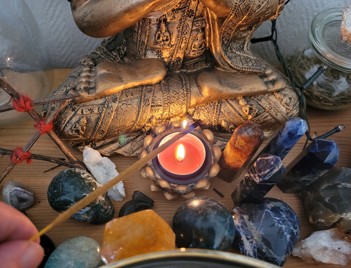 close view of altar with red tea light, an incense stick being lit and crystals and spiritual tools made of natural resources.