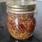 A jar with dried St. John's Wort soaked in tincture. The red colour is visible in the liquid.